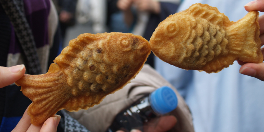 Twee mensen houden taiyaki-wafels omhoog, zodat het lijkt alsof de vissen kussen