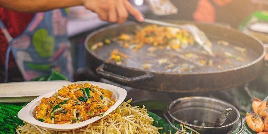 Vrouw maakt Pad Thai op een markt in Bangkok
