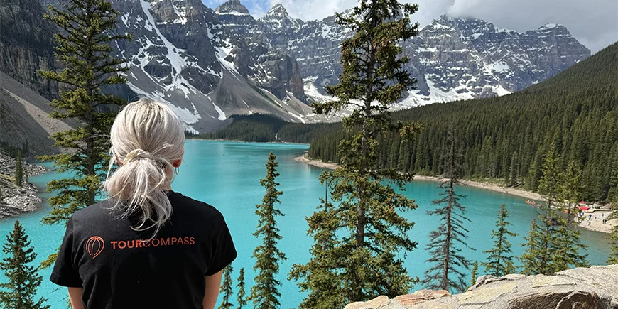 Vrouw in TourCompass-T-shirt kijkt uit over het water bij Lake Louise in Canada